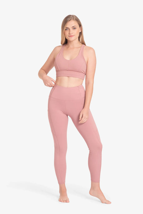 Mujer con conjunto deportivo rosa pastel, top deportivo y leggings ajustados, fondo blanco