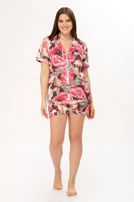 Mujer sonriente con pijama corto floral rosa y marrón sobre fondo blanco, moda cómoda para dormir