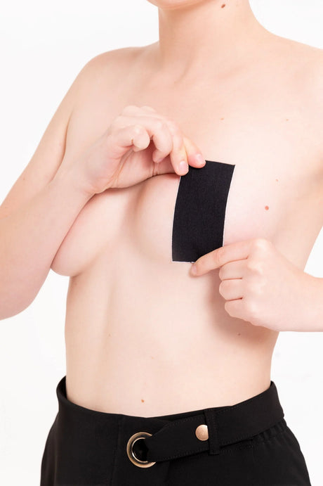 Persona sin camisa aplicando parche adhesivo negro en el pecho, fondo blanco, ropa negra